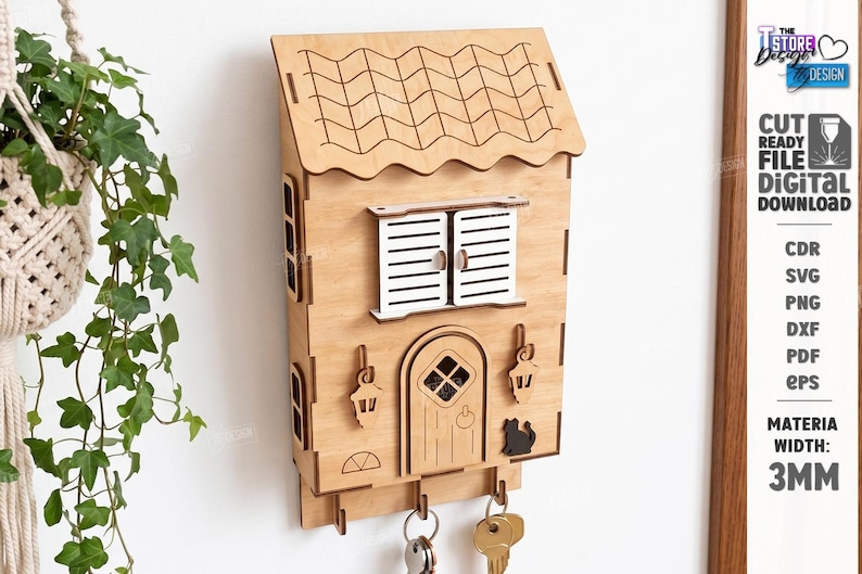 May include: A light-colored wooden wall-mounted key holder shaped like a house with a tiled roof, white shutters, a central door, two hanging lanterns, and a small black cat silhouette. Three metal hooks at the bottom hold several silver keys.