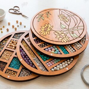 May include: Wooden craft organizer with multiple compartments filled with beads in various colors. The top lid features a laser-cut floral design. Other craft supplies, including scissors and thread, are also visible.