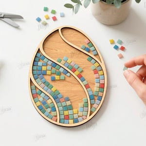 May include: Wooden egg-shaped mosaic craft kit with colorful tiles. The kit includes a wooden base, mosaic tiles in various colors, and mosaic glue. Scissors and a tube of glue are also visible.