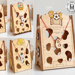 Puede incluir: Una colección de cinco diseños de madera cortados con láser, cada uno con un tema único y elementos decorativos. Los diseños incluyen cestas de Pascua, un campo de fútbol y otros motivos lúdicos. El texto "CUT READY FILE" y "5 DESIGNS" es visible.