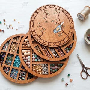 May include: Wooden bead organizer with multiple compartments filled with colorful beads. The top lid features a bird and branch design. Additional items include tweezers, scissors, and a small bowl with beads.