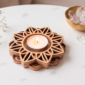 May include: A layered wooden tea light candle holder with a geometric flower-shaped cutout design. The light-colored wood features a stacked construction holding a single white tea light candle with a lit flame in the center of the structure.