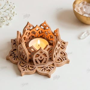 May include: A light brown wooden lotus flower candle holder with intricate laser-cut petal designs. A small round tea light candle with a warm yellow flame sits in the center. The text on the right reads: The Store Design, Cut Ready File Digital Download, CDR, SVG, PNG, DXF, PDF, EPS, Compatible with any material thickness.