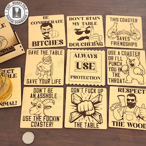 May include: A collection of ten wooden coasters with humorous phrases and illustrations. The coasters are square and feature laser-cut designs, including text like "Protect the Table" and "Save Your Life". A wooden box and a bottle are also visible.