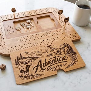 K&ouml;nnte beinhalten: Cribbage-Brett aus Holz mit tierf&ouml;rmigen Stiften und einem passenden Kartenhalter aus Holz mit der Gravur "Adventure Awaits". Enth&auml;lt W&uuml;rfel und eine Spielkarte.