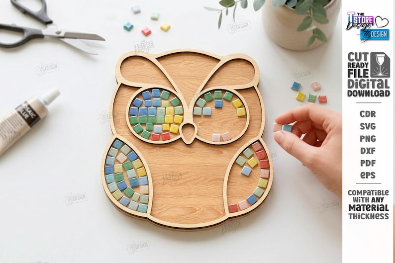 May include: Wooden owl-shaped mosaic tray with colorful square tiles. The tray has a light brown wood grain finish. The eyes and feathers of the owl are designed to hold the mosaic tiles. A hand is placing a tile.