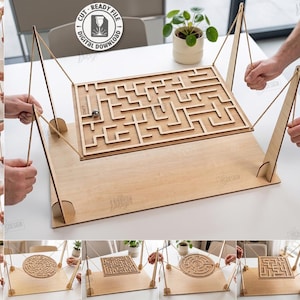 May include: A wooden labyrinth game board suspended by strings on a base, featuring a metal ball bearing. The set includes 10 laser cut designs in digital file formats like SVG, CDR, and DXF for 3mm material width, as indicated by the text.