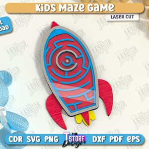 May include: A laser-cut wooden rocket ship maze game for kids. The rocket is red, blue, and yellow, with a maze design in the center. The image also includes a blue teddy bear and wooden balls.