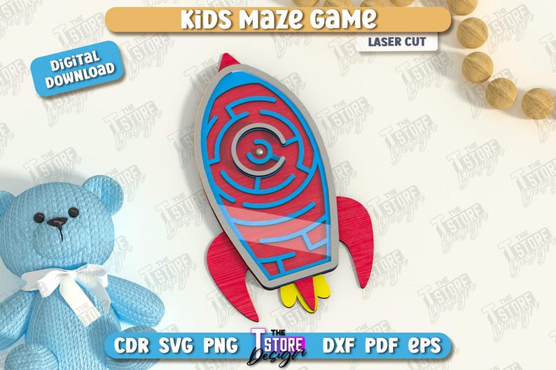 May include: A laser-cut wooden rocket ship maze game for kids. The rocket is red, blue, and yellow, with a maze design in the center. The image also includes a blue teddy bear and wooden balls.
