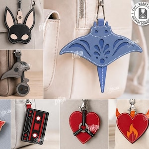 Peut inclure: Une collection de dix porte-clés en cuir découpés au laser, incluant un trèfle vert, un masque de lapin noir, une plume, une feuille de monstera, un masque de médecin de peste, une raie bleue, des lèvres rouges, une cassette, un cœur rouge et un cœur avec des cornes de diable orange.