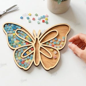 May include: A wooden butterfly-shaped tray with a mosaic tile design. The mosaic tiles are in shades of blue, green, yellow, and red. The tray is surrounded by scattered tiles, scissors, and a tube of glue. The image also includes the text "CUT READY FILE DIGITAL DOWNLOAD".