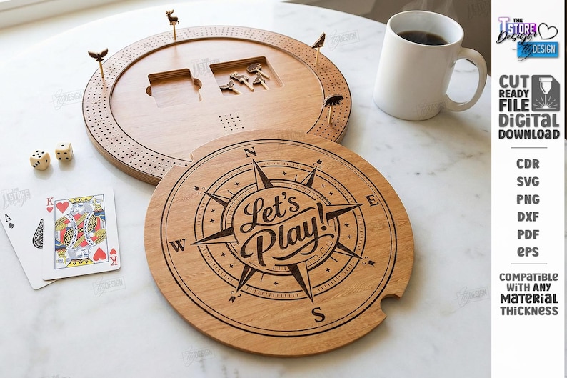 K&ouml;nnte beinhalten: Ein h&ouml;lzernes Cribbage-Brett mit Stiften, W&uuml;rfeln und Spielkarten. Das Brett hat ein kreisf&ouml;rmiges Design mit einer Windrose und den Worten "Let's Play!" auf dem Deckel eingraviert. Eine wei&szlig;e Tasse ist ebenfalls vorhanden.