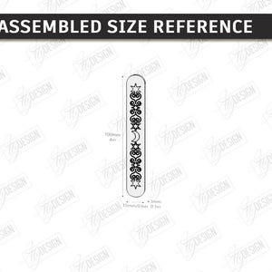 Op de afbeelding: Een verticaal designelement met afgeronde uiteinden, met een decoratief patroon van sterren, manen en krullen. Het ontwerp is 10 cm lang en 3 mm breed. De tekst "ASSEMBLED SIZE REFERENCE" staat bovenaan.