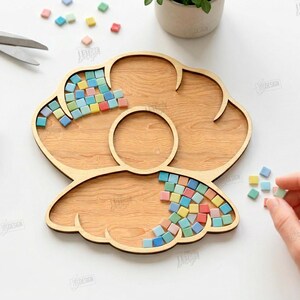 May include: A wooden craft tray with a flower-like design, partially filled with colorful mosaic tiles. Scissors and a tube of adhesive are nearby. The image also includes text that says "CUT READY FILE DIGITAL DOWNLOAD".