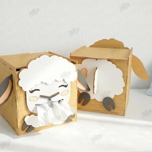 May include: Two wooden tissue box holders shaped like sheep. The sheep have white wool, gray ears, and black eyes. One box has tissues coming out. The boxes are light brown and have a 3mm width.