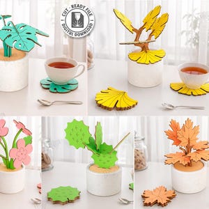 May include: A collection of five laser-cut wooden plant designs, including a monstera, a tree, flowers, a cactus, and autumn leaves, each in a white pot. The image also shows coasters, spoons, and teacups. The text on the image says "CUT READY FILE" and "5 DESIGNS".