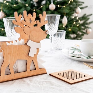 May include: A light-colored wooden napkin holder shaped like a reindeer with a white scarf, featuring a grid-patterned side panel. Beside it lies a square wooden coaster with a matching grid cutout design, both crafted from 3mm thick material.