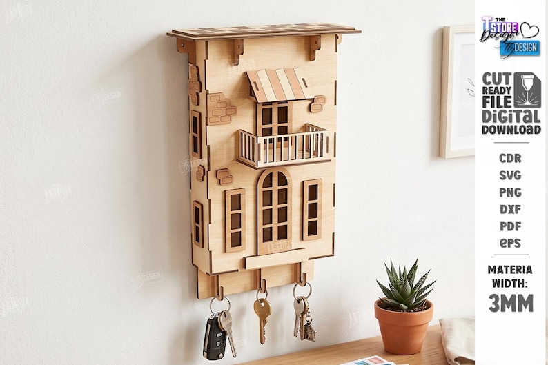 May include: A light-colored wooden wall-mounted key holder shaped like a building facade with a balcony, awning, and windows. It features three metal hooks at the bottom for hanging keys. The design includes laser-cut details and a 3mm material width.