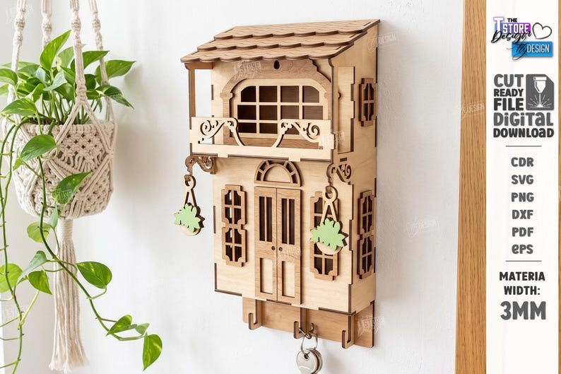 May include: A laser-cut wooden wall-mounted key holder shaped like a two-story house with a balcony, windows, and hanging plant details. The structure features a shingled roof, a central door, and three hooks at the bottom for keys. Material width: 3mm.