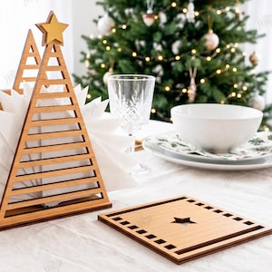 May include: A wooden napkin holder shaped like a Christmas tree with a star topper, holding white napkins, alongside a square wooden coaster with a star cutout. The design features a 3mm material width, with digital file formats listed.