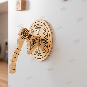 Puede incluir: Decoraci&oacute;n de pared de madera con hacha y escudo vikingos. El hacha y el escudo son de madera clara con intrincados dise&ntilde;os negros grabados. El hacha est&aacute; montada delante del escudo. El texto "CUT READY FILE DIGITAL DOWNLOAD" es visible.