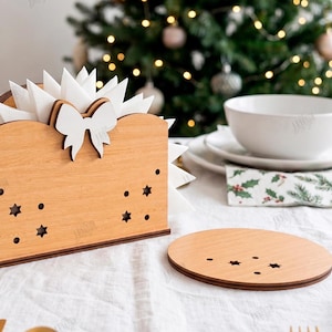 May include: A light brown wooden napkin holder featuring a white bow cutout at the top and star-shaped perforations on the sides, accompanied by a matching round wooden coaster with small star cutouts, both with a material width of 3mm.