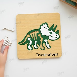 K&ouml;nnte beinhalten: Holzpuzzle mit einem gr&uuml;nen und wei&szlig;en Triceratops-Dinosaurier-Design. Das Puzzle enth&auml;lt eine Holzbasis mit der Dinosaurierkontur und separaten Teilen. Das Wort "Triceratops" ist auf der Basis aufgedruckt.