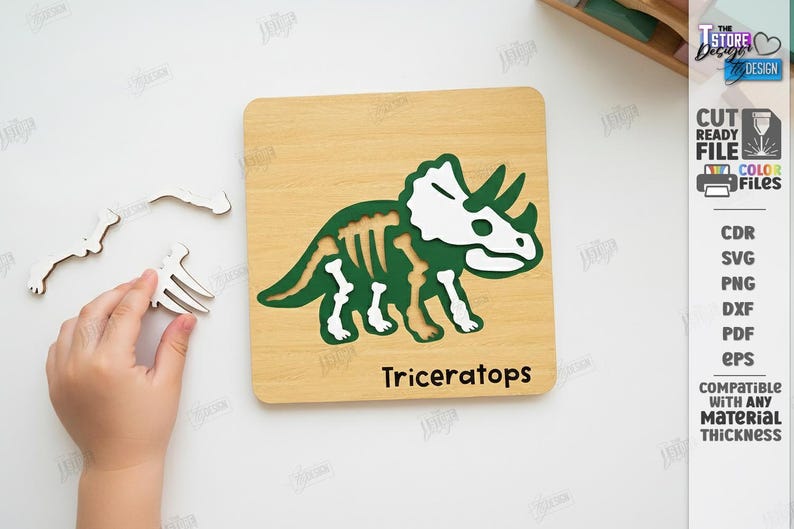 K&ouml;nnte beinhalten: Holzpuzzle mit einem gr&uuml;nen und wei&szlig;en Triceratops-Dinosaurier-Design. Das Puzzle enth&auml;lt eine Holzbasis mit der Dinosaurierkontur und separaten Teilen. Das Wort "Triceratops" ist auf der Basis aufgedruckt.