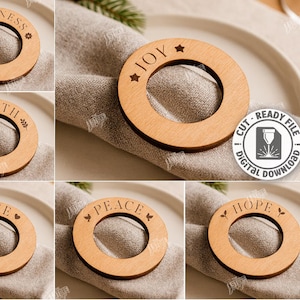 Op de afbeelding: Houten servetringen met lasergesneden ontwerpen. Elke ring heeft een ander woord: Geluk, Gezondheid, Vreugde, Liefde, Vrede en Hoop. De ringen worden gepresenteerd op een neutraal gekleurde servet.