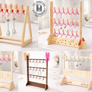 以下が含まれることがあります： さまざまなデザインの木製イヤリングディスプレイスタンド。ピンクのハート型のハンガーが付いているものもあれば、イヤリング用の穴が並んでいるものもあります。スタンドは明るい色の木材でできており、レーザーカットに適しています。画像には「5 Designs」というテキストが含まれています。