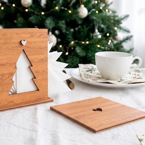 May include: A light brown wooden napkin holder featuring a cutout Christmas tree shape and a small heart detail, accompanied by a matching flat wooden square with a heart cutout. The material width is clearly labeled as 3MM on the side.