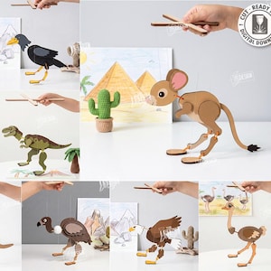 Puede incluir: Una colección de diez marionetas de madera cortadas con láser que representan varios animales, incluyendo un canguro, un dinosaurio, un flamenco, un ganso y un águila. Cada marioneta está articulada con hilos unidos a una barra de control.