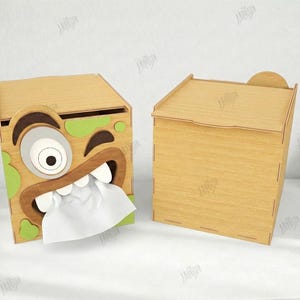 May include: Two wooden tissue box holders. One features a cartoon monster face with green accents and white tissue protruding. The other is a plain wooden box. The text on the right says "CUT READY FILE" and "MATERIAL WIDTH: 3MM".