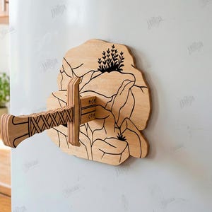 Puede incluir: Una pieza decorativa de pared de madera con un dise&ntilde;o de espada estilizada. La pieza es de color marr&oacute;n claro con detalles negros grabados, incluyendo una escena de monta&ntilde;a y el texto "ROK OPA". El dise&ntilde;o est&aacute; montado sobre una superficie blanca.