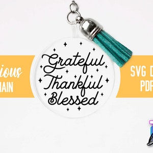 Pu&ograve; includere: Un portachiavi circolare bianco con il testo "Grateful Thankful Blessed" in scrittura nera. Il portachiavi ha un nappina turchese.