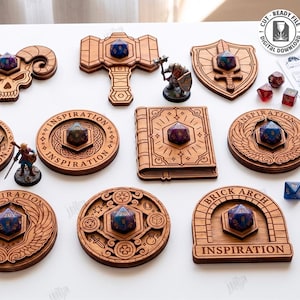 Puede incluir: Una colección de 10 diseños de madera cortados con láser, que incluyen una calavera, un martillo, un escudo y un libro, cada uno con un dado de múltiples caras. Los diseños son de varias formas y tamaños, con la palabra "INSPIRATION" en algunos. La imagen también incluye una figura en miniatura y dados.