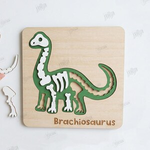 K&ouml;nnte beinhalten: Holzpuzzle eines Brachiosaurus-Dinosauriers mit gr&uuml;nen und wei&szlig;en Details. Das Puzzle zeigt ein Dinosaurierskelett-Design und das Wort "Brachiosaurus". Enth&auml;lt separate Puzzleteile. Ideal f&uuml;r Kinder.