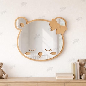 May include: A bear-shaped mirror with a wooden frame and bow, featuring closed eyes and a nose. The mirror is mounted on a white wall. The text "CUT READY FILE" and "COLOR FILES" is visible. The material width is 3mm.