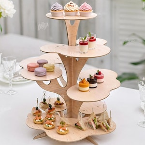 May include: A multi-tiered wooden dessert stand with a tree-like design, holding cupcakes, macarons, and mini desserts. The stand is made of light-colored wood and is filled with various treats. The text "CUT READY FILE DIGITAL DOWNLOAD" is visible.