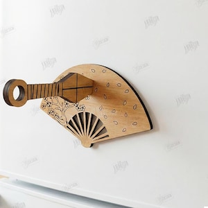Puede incluir: Un im&aacute;n de madera en forma de abanico con un mango y recortes florales y geom&eacute;tricos decorativos. El abanico es de color marr&oacute;n claro con un borde marr&oacute;n oscuro y est&aacute; adherido a una superficie blanca. El texto "CUT READY FILE DIGITAL DOWNLOAD" es visible.