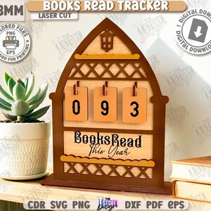 Puede incluir: Un "Books Read Tracker" de madera con los n&uacute;meros "093" mostrados. El rastreador tiene un marco marr&oacute;n y un fondo de madera clara. El texto "Books Read This Year" est&aacute; debajo de los n&uacute;meros. La imagen tambi&eacute;n incluye una suculenta en una maceta blanca.