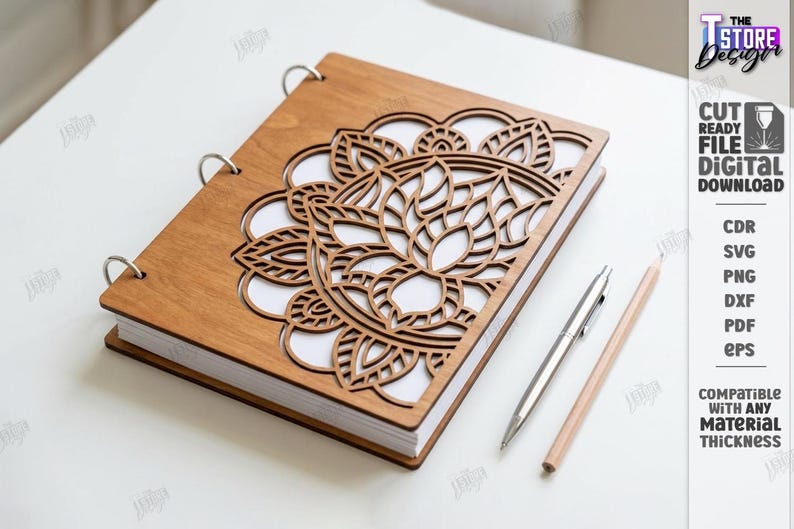May include: A wooden notebook with a laser-cut floral design on the cover. The notebook is open, revealing white pages. A silver pen and a wooden pencil are placed beside the notebook. The notebook is held together with metal rings.