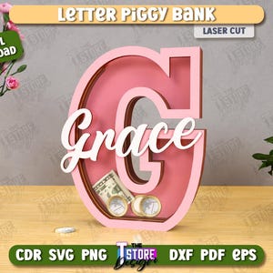 Puede incluir: Una hucha de madera rosa con forma de la letra "G" con el nombre "Grace" en escritura blanca. El banco contiene dinero y monedas. Las palabras "Letter Piggy Bank" y "Laser Cut" est&aacute;n en la parte superior.