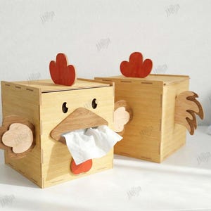 May include: Two wooden tissue box holders shaped like chickens. Each box has a red comb, a wooden beak, and a red wattle. The boxes are made of light-colored wood and have a 3mm width. The boxes are cut-ready files.