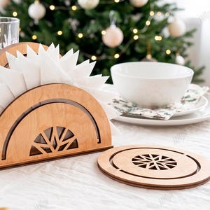 May include: A light-colored wooden napkin holder with a semi-circular design and a matching circular coaster, both featuring a geometric star-like cutout pattern. The material width is 3mm. The set is displayed on a white tablecloth with white napkins.