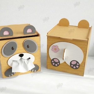 May include: Two wooden tissue box holders, one with a panda face design and the other with a bear butt design. The panda box has gray eyes and paws, with tissue paper coming out of its mouth. The bear box has a pink flower and paw prints.
