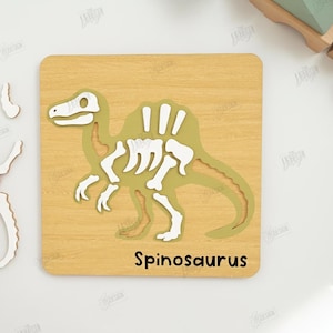 K&ouml;nnte beinhalten: Holzpuzzle eines Spinosaurus-Dinosauriers mit wei&szlig;en Knochen und einem gr&uuml;nen K&ouml;rper. Die Puzzleteile sind getrennt, mit dem Wort "Spinosaurus" auf der Basis. Design-Dateiformate sind ebenfalls enthalten.