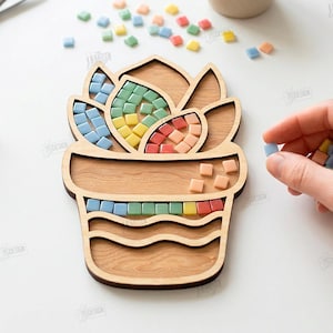 May include: Wooden succulent-shaped mosaic tile holder with colorful square tiles. The holder is made of light-colored wood and has sections for the tiles. The image also shows a tube of glue and scissors.