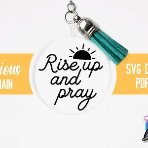 Pu&ograve; includere: Un portachiavi rotondo e trasparente con un sole nero e il testo "Rise up and pray". Il portachiavi ha un pon pon turchese.