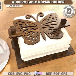 May include: Wooden table napkin holder with a laser-cut butterfly design. The holder is made of dark brown wood and holds a stack of white napkins. The text "WOODEN TABLE NAPKIN HOLDER" is visible.